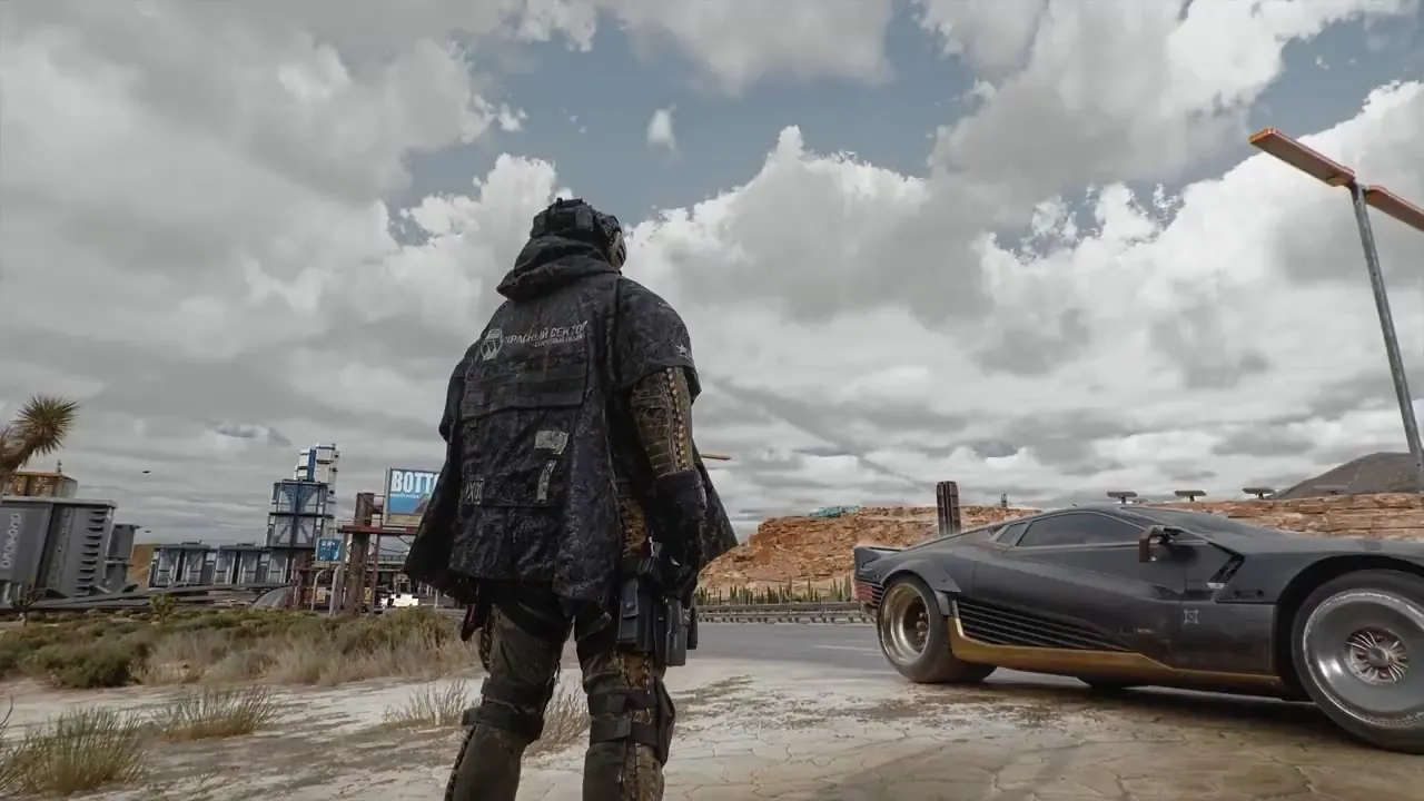 V stands beside a black Quadra on a daytime Badlands road, facing away from the camera toward open desert