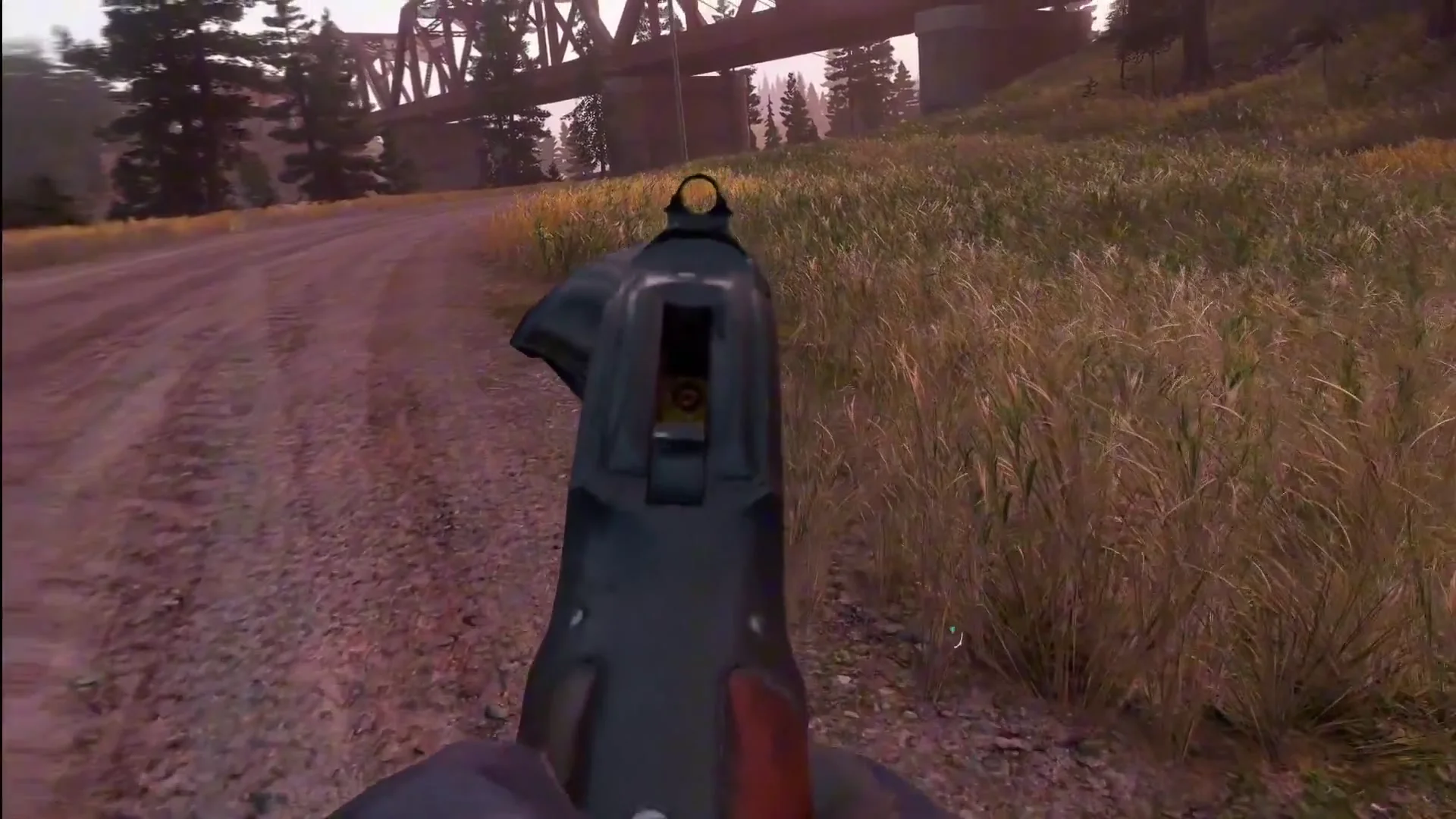 A gloved hand holding a gun in first person on a dirt road toward a truss bridge