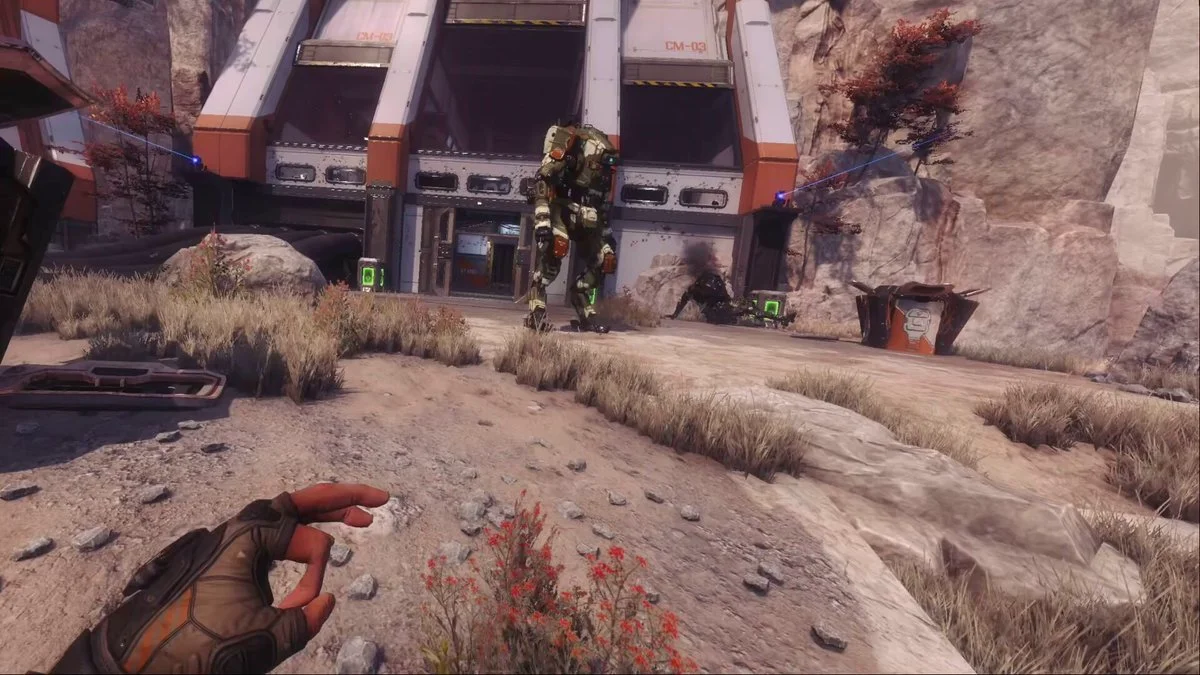 A gloved first-person hand held open on a desert path, with a Titan standing in front of a hangar