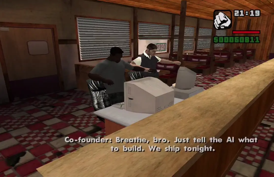 CJ seated at a diner desk with his co-founder behind one beige CRT monitor, with the co-founder subtitle about telling the AI what to build