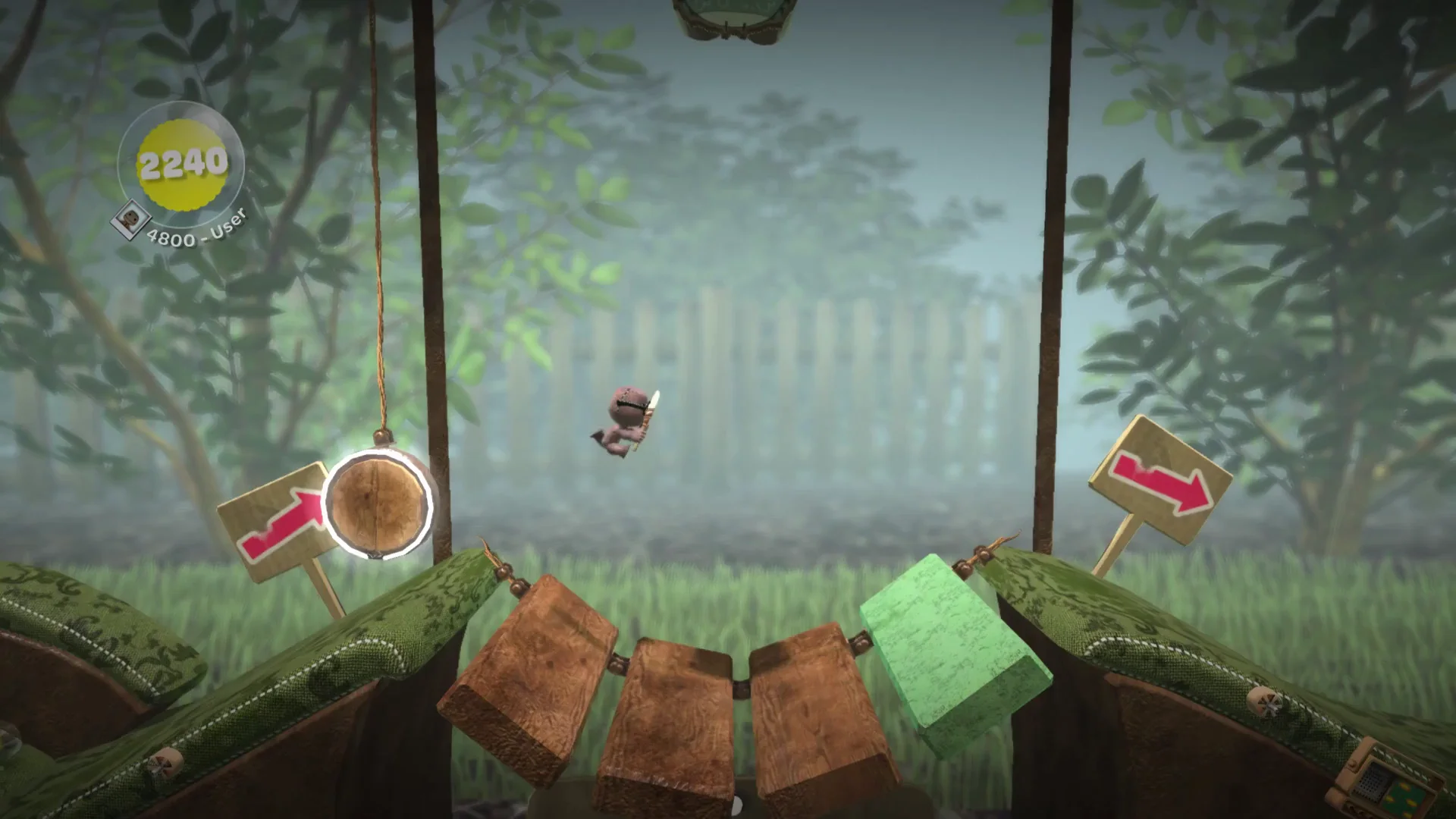 Sackboy mid-air over a sponge-block bridge between wooden signs with red arrows