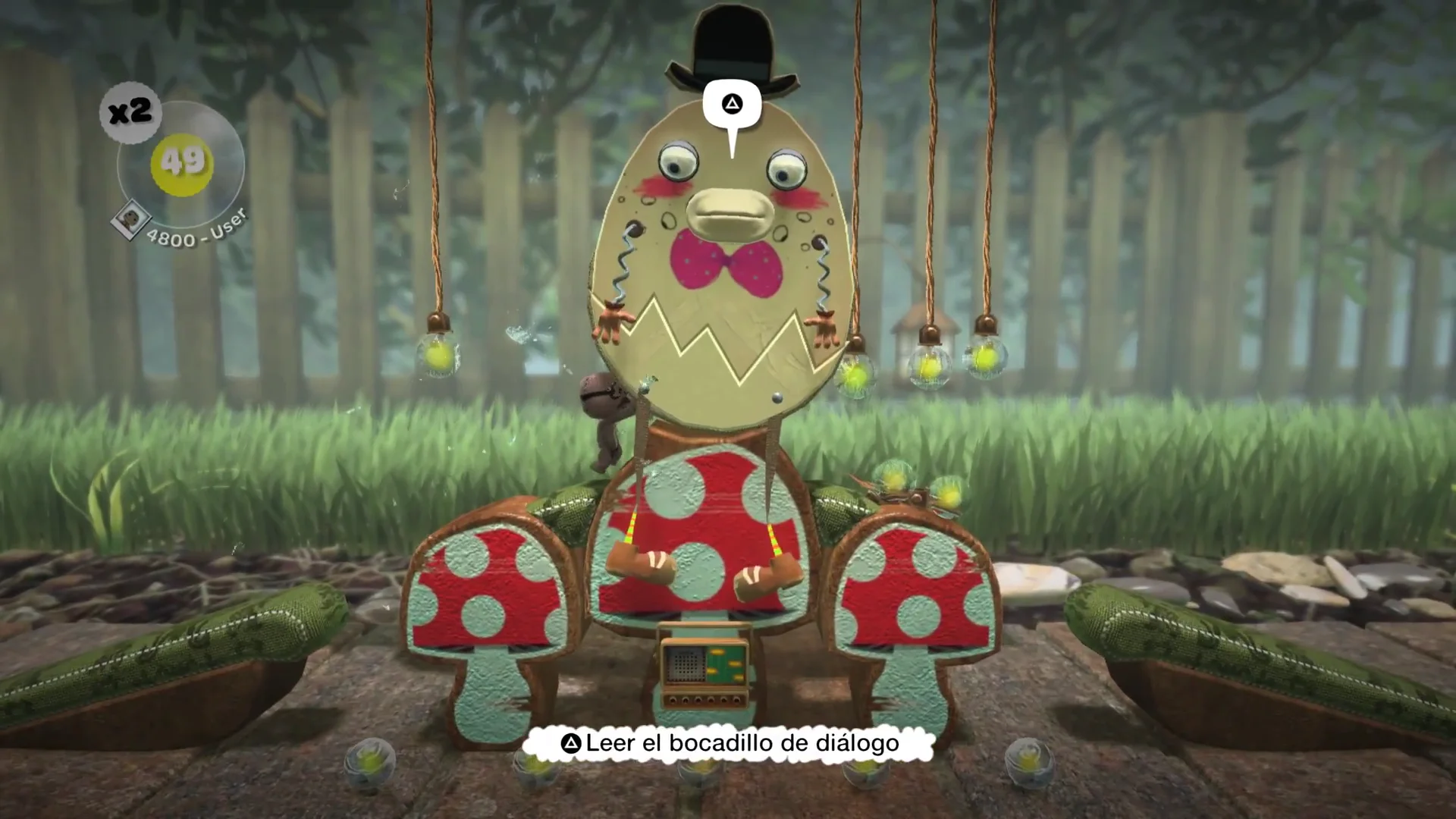 Large top-hatted cardboard character on red mushroom cutouts in a garden level, with a Leer el bocadillo de diálogo prompt below